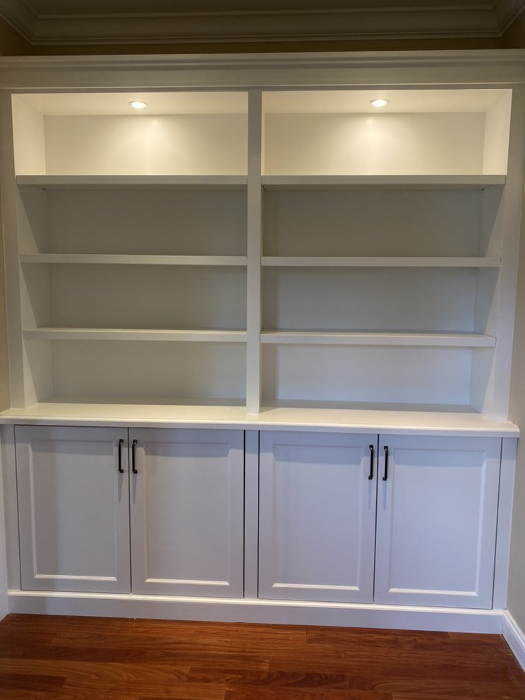 White built-in bookcase with lit upper shelving and shaker base cabinets