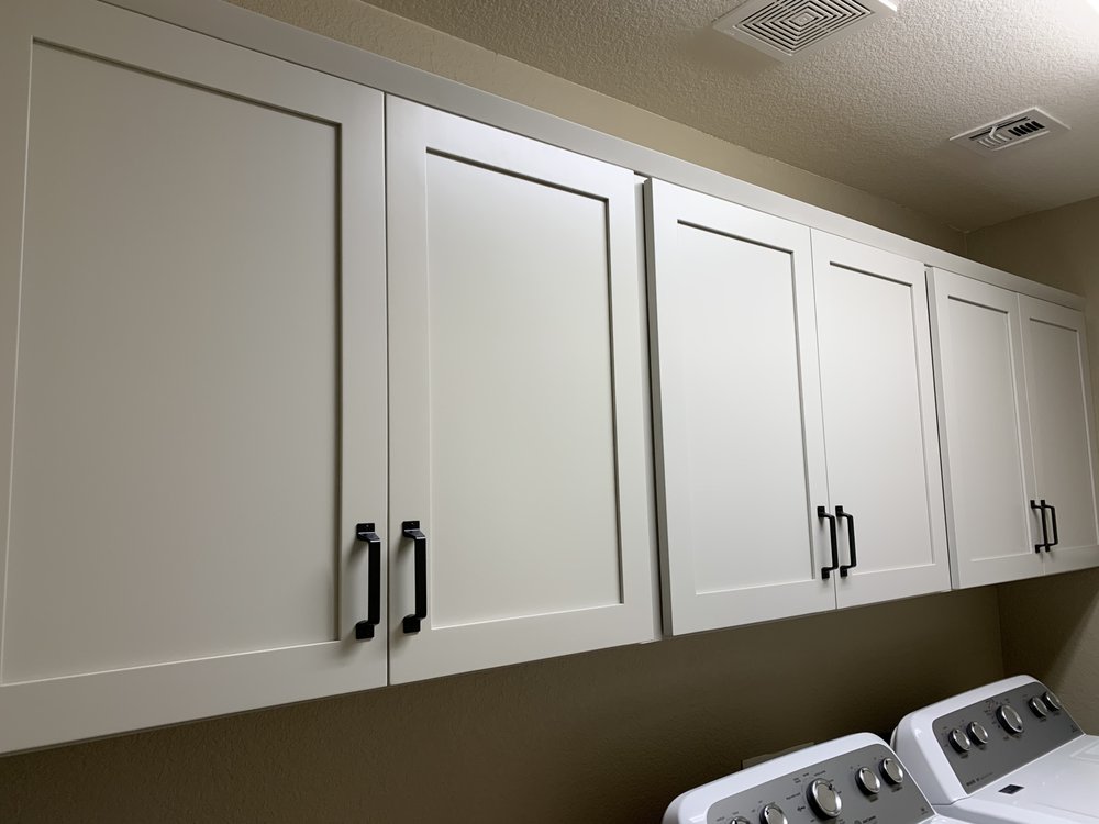 White shaker upper cabinets with black pulls installed above laundry machines