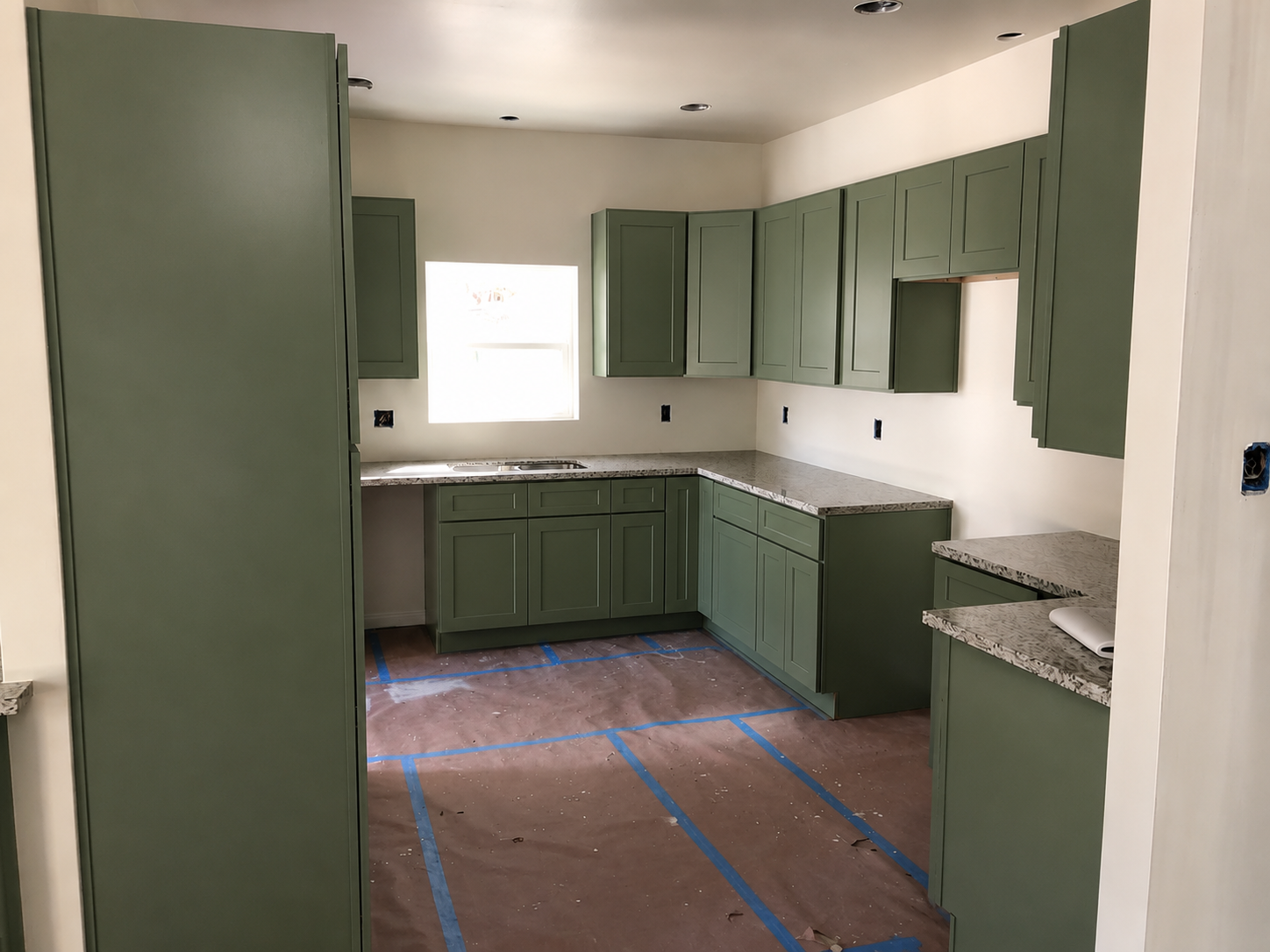 Sage green shaker kitchen cabinets with speckled granite countertops mid-installation