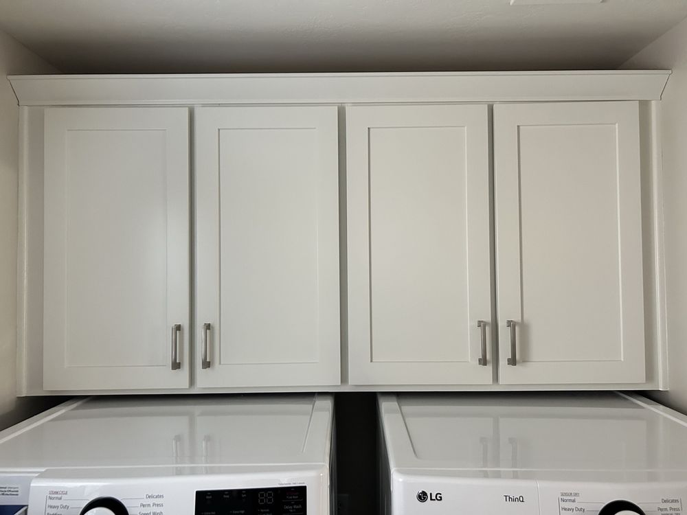 White shaker laundry cabinets with crown molding and brushed nickel pulls
